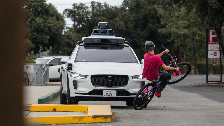 A cyclist does a wheelie in front of a Waymo