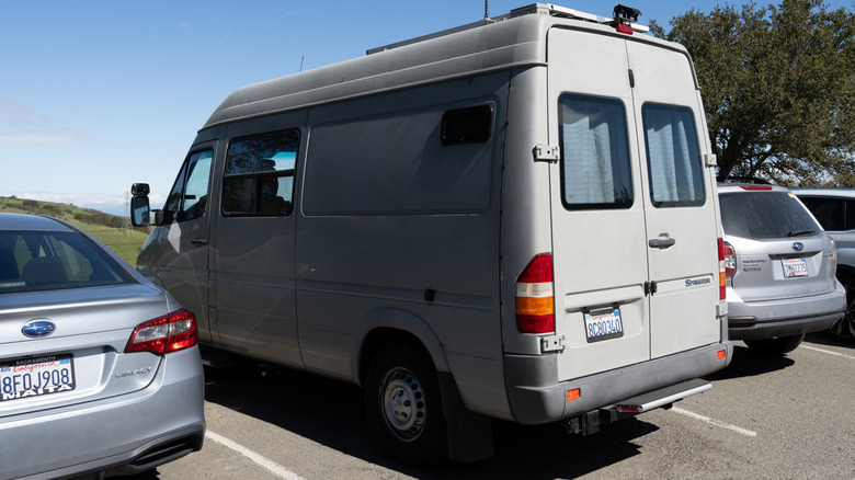 A Van Lifer Sprinter van among cars in a traditional parking lot