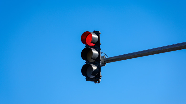 A black traffic light showing a red light against a blue sky.