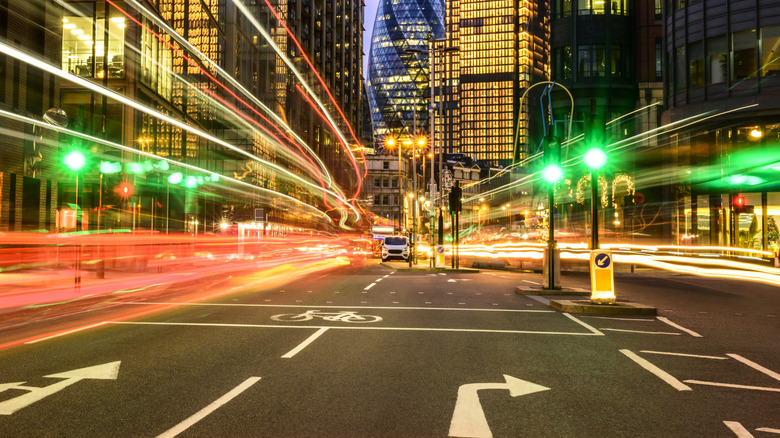 A long-exposure capture of cars running through a downtown city center with green lights ahead.