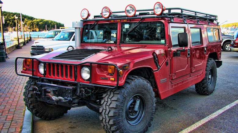 A red Hummer H1 parked up on a parking bay, with a bay and other cars in the background