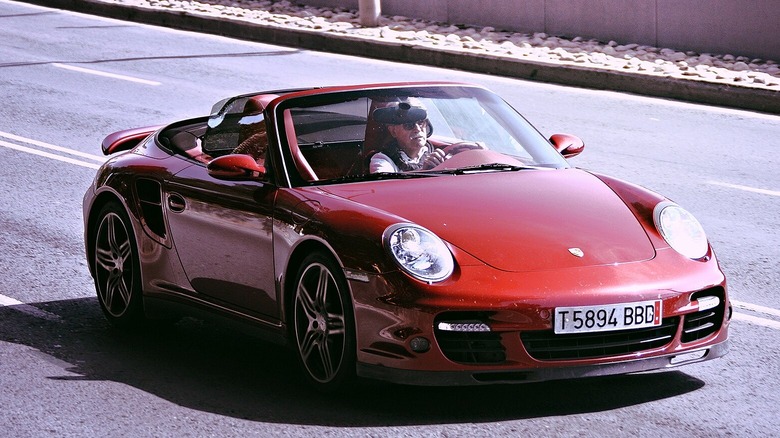 A red Porsche 997 Turbo Cabriolet driving on a public road