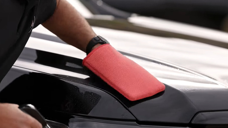 A red clay mitt being used on the hood of a black car