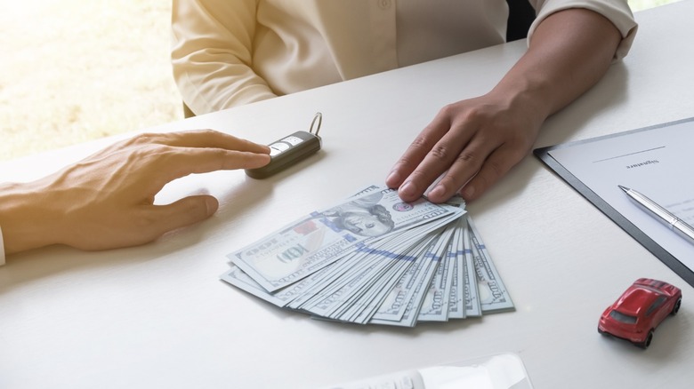 Money and key fob being exchanged on desk where a red toy car is sitting