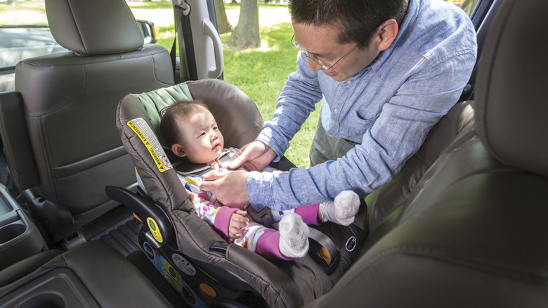 A man buckling a child into a rear-facing car seat in the back of a minivan