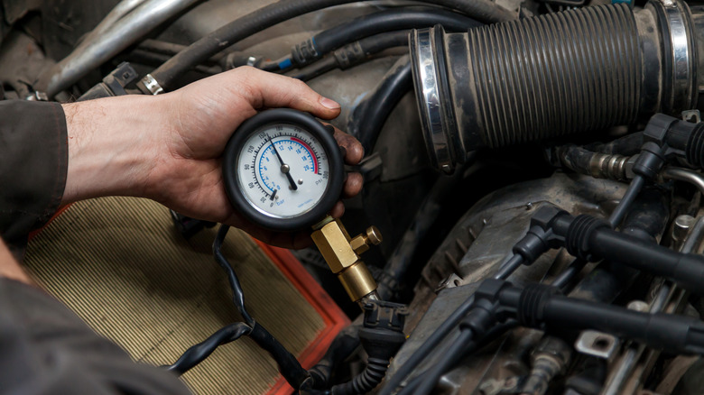 A hand holding a compression tester that's attached to an engine cylinder.