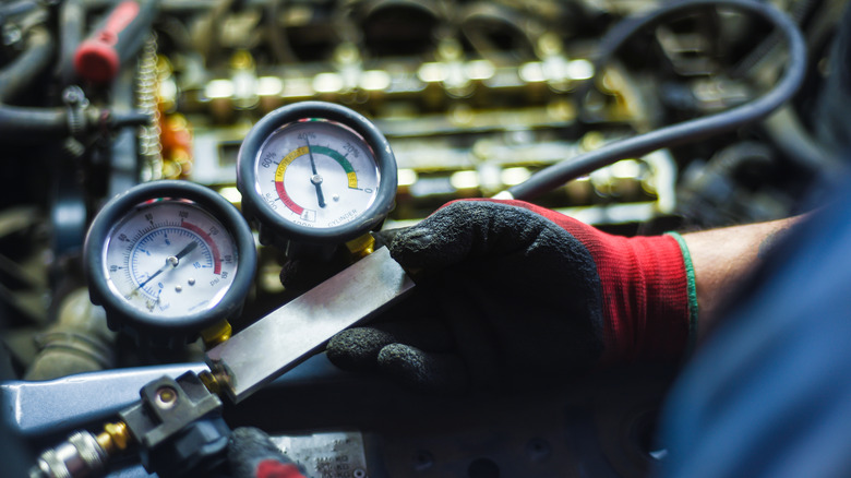 A person utilizing a leak-down tester to check an engine's cylinder for leak-down.