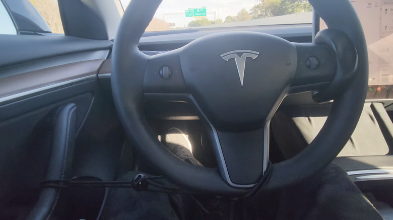 A Tesla in Full Self-Driving mode with defeat devices on the steering wheel to fool the car into thinking the driver's hands are on it