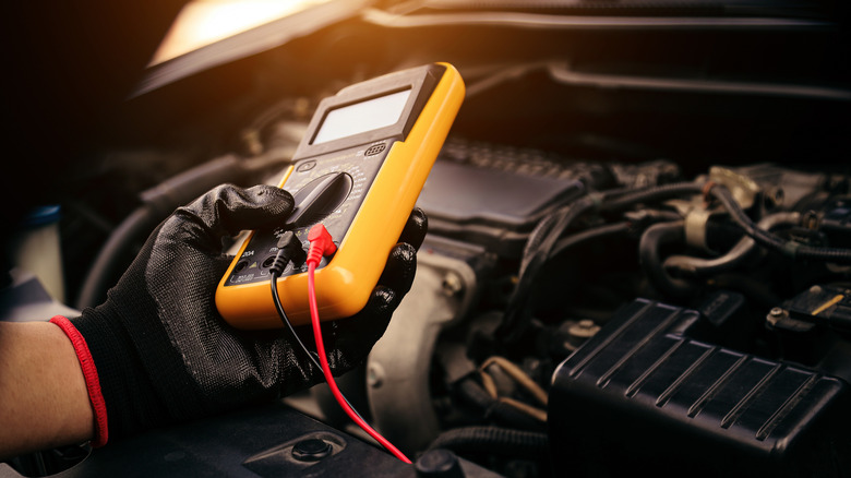 A car mechanic checking a car with a multimeter.
