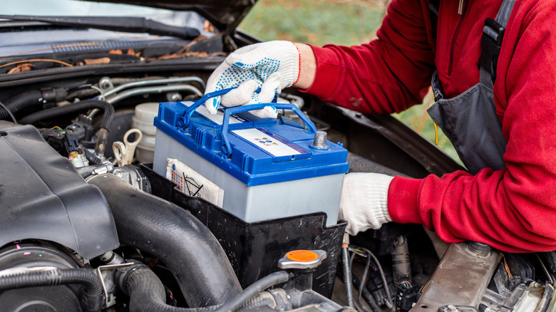 A man installs a new battery under the hood of a car.