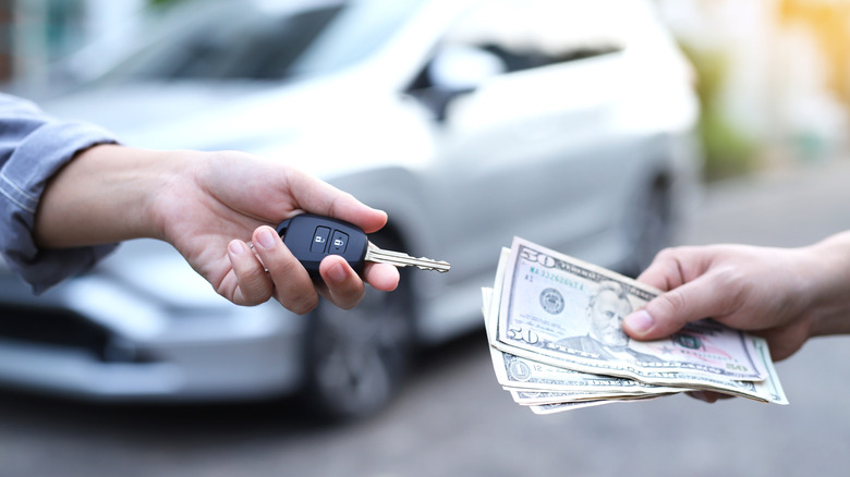 Close up hands trading money for car key with vehicle in background