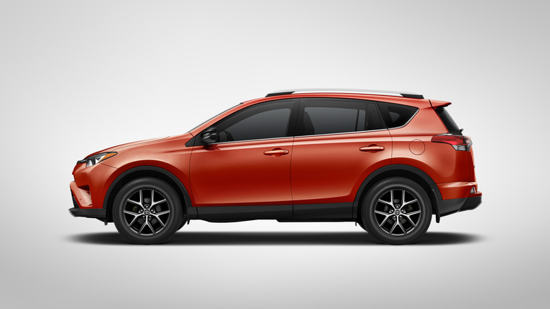 A driver's-side profile studio shot of an orange-red 2016 Toyota RAV4 SE
