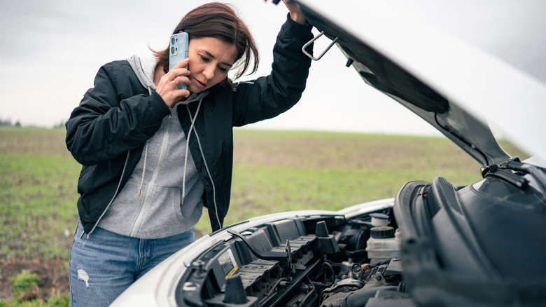 A woman using her phone while holding a car's hood up