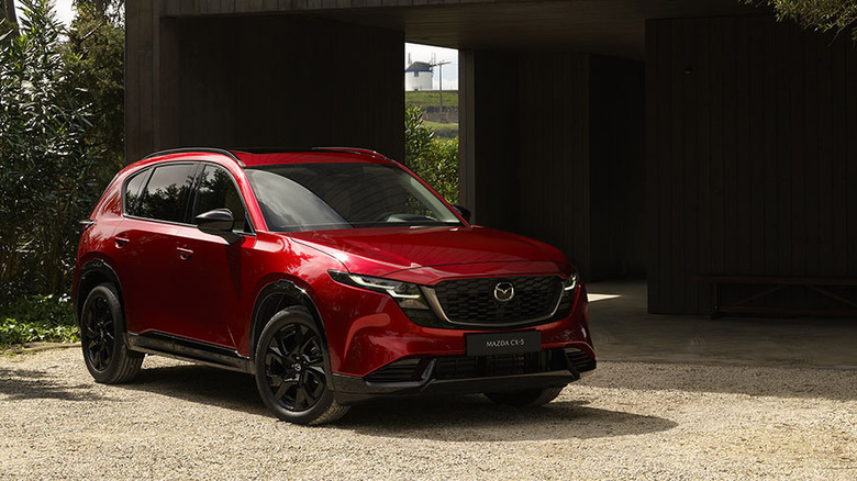 A red 2026 Mazda CX-5 on gravel and in front of a garage.