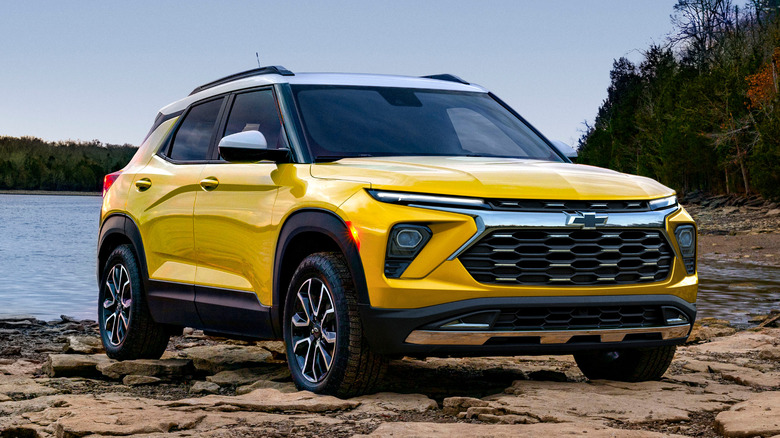 A yellow Chevrolet Trailblazer ACTIV parked on top of rocks near a lake.