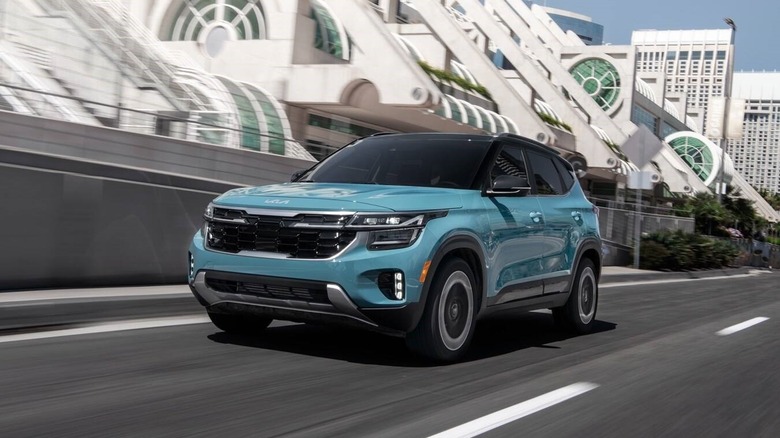 A blue Kia Seltos driving on a highway through a modern city.