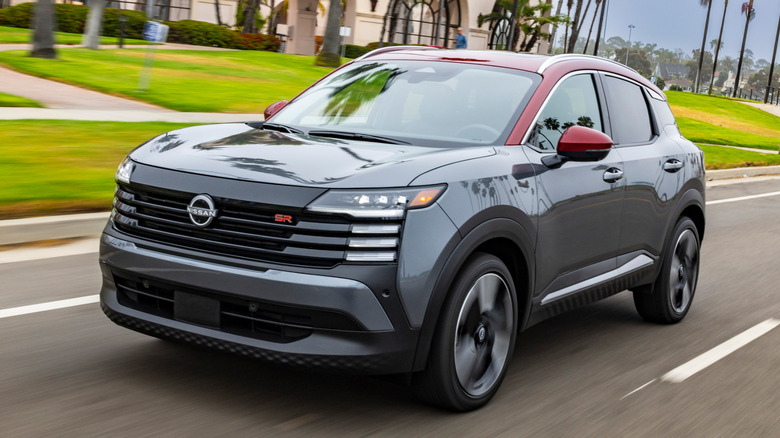 A grey Nissan Kicks with red accents driving on a road.