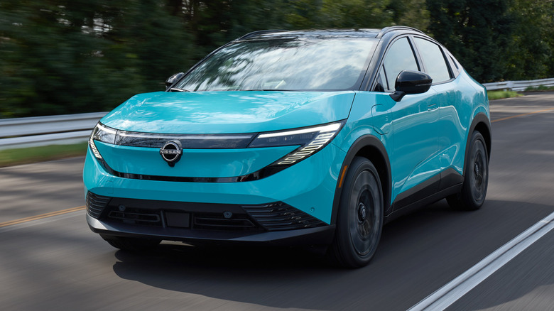 A blue Nissan Leaf driving down a highway with trees in the background.