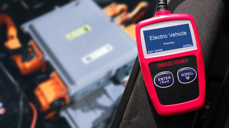 A handheld fault code scanner, running a vehicle diagnostic on an electric car, shown in the background
