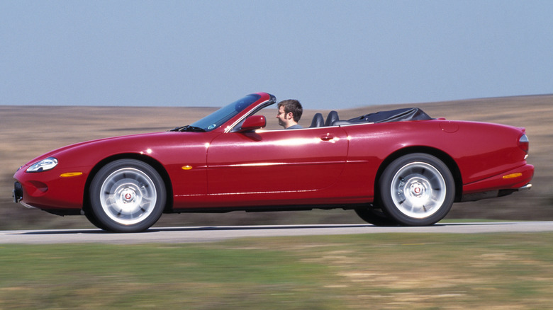 A person driving a red 2000 Jaguar XKR convertible