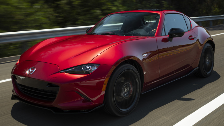 Red Mazda MX-5 Miata RF driving on a road with a metal guardrail on the side