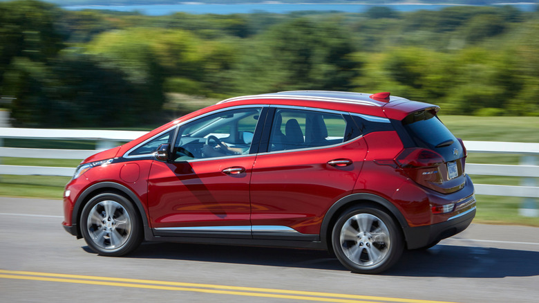 A red Chevrolet Bolt on a roadway in front of a white fence