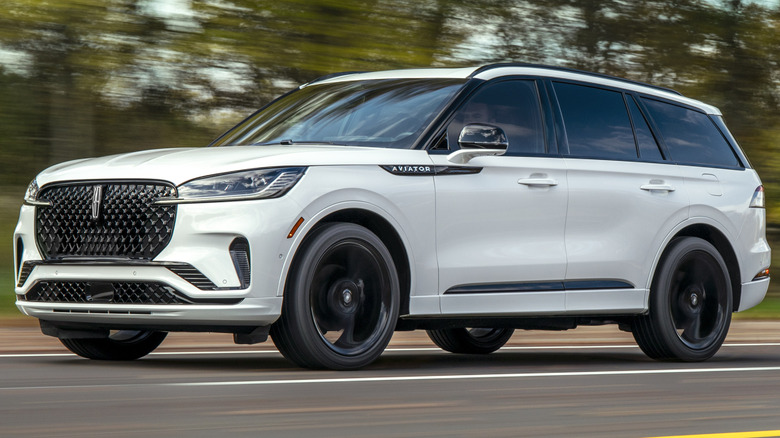 Pristine white 2025 Lincoln Aviator Reserve driving down a road with trees in the background