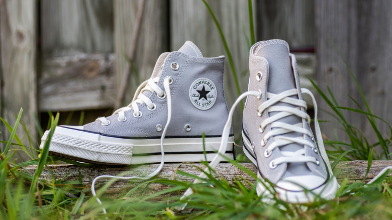 A pair of high top Converse sneakers sitting on a piece of wood in tall grass