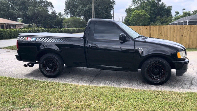 A black Ford F-150 sits in a driveway with a checkered stripe running along the bed featuring NASCAR graphics.