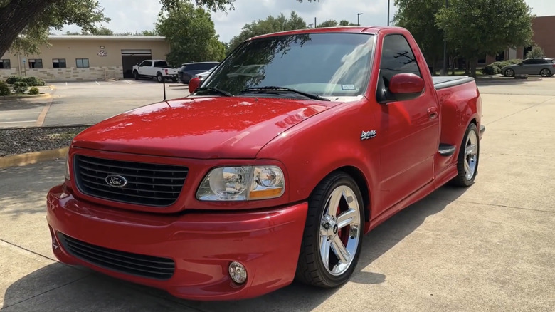 A red F-150 Lighting parked under a tree is photographed from the driver's side front angle.