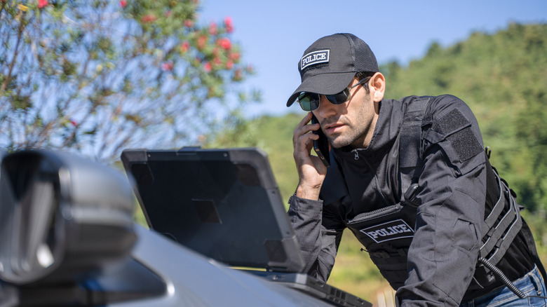 Stock image of a police officer on a laptop outside with a serious look.