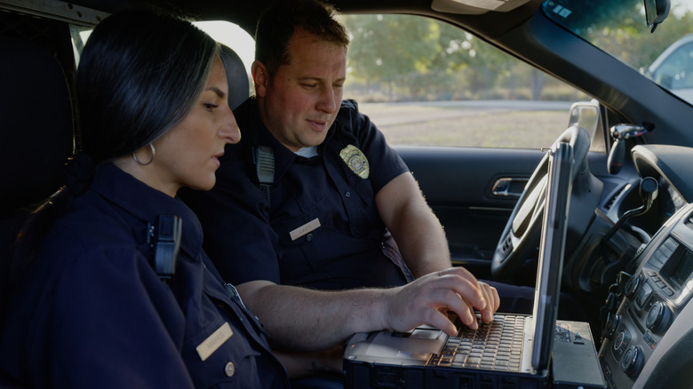 Stock image of two police officers on a laptop in their car.