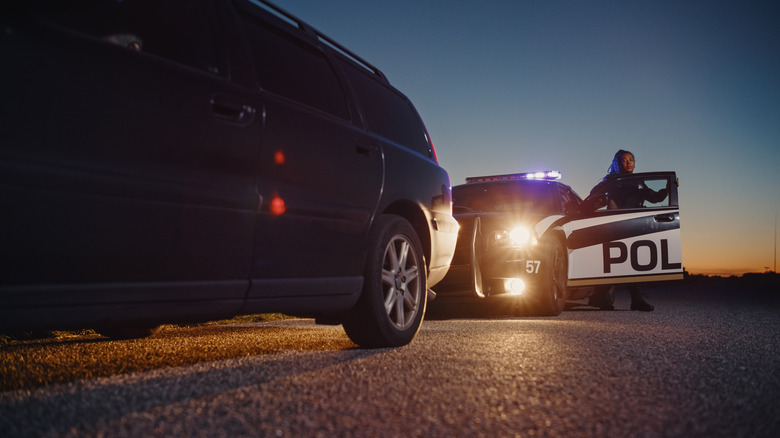 A police officer getting out of her car after pulling over a station wagon on a road at sunset