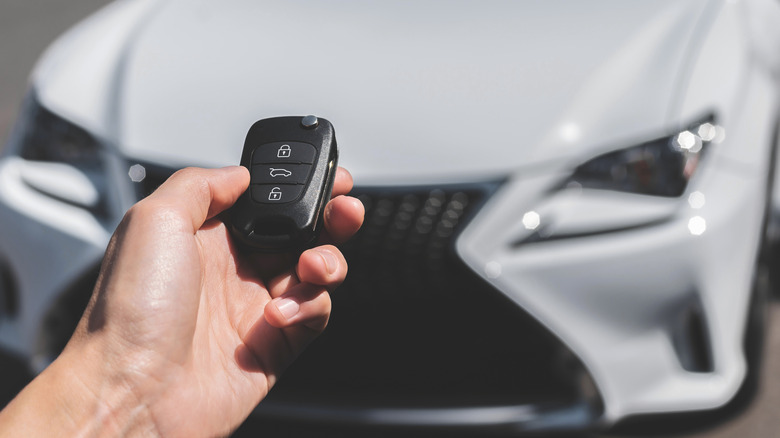 A person holding a key fob unlocking a Lexus.