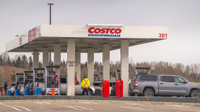 a bust costco gas station with sevveral cars at the pumps and a person in a yellow vest. The sky is overcast