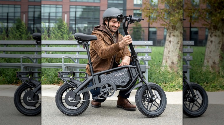 A person kneeling down next to a Jetson Bolt Pro Max Electric Bike with a park bench and a tree in the background