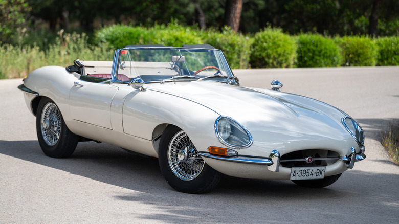 A white Jaguar E-Type parked outside with its roof down.