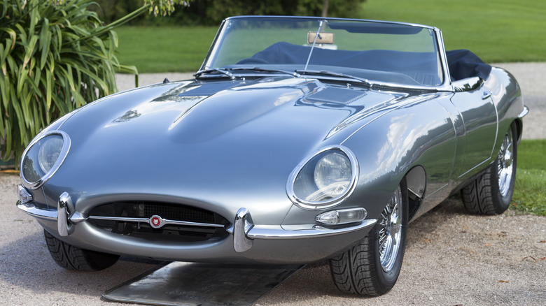 A silver Jaguar E-Type roadster parked outside.