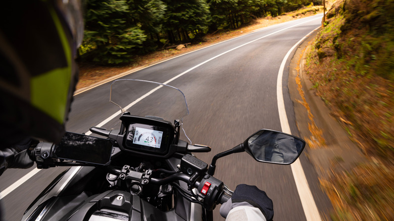 A motorcycle rider cruising on a two-lane country road.