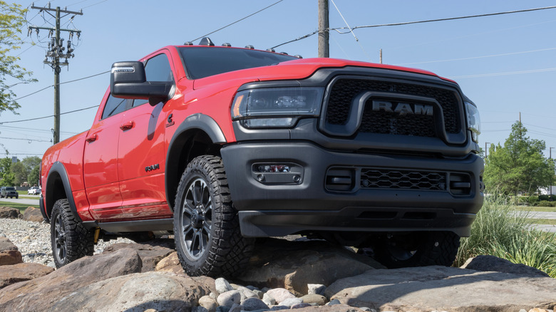 A red Ram 2500 off-road pickup truck model driving over rocks next to grass, power lines, and trees