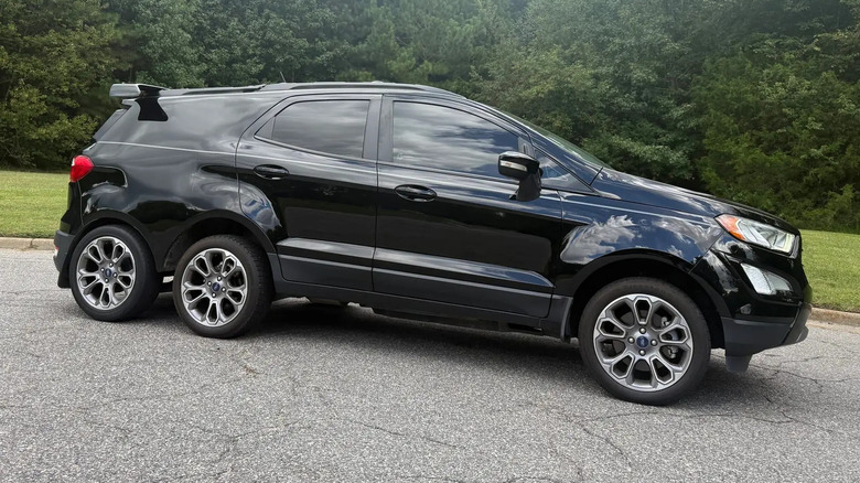 A side view of the black EcoSport six-wheeler parked on asphalt in front of grass and trees