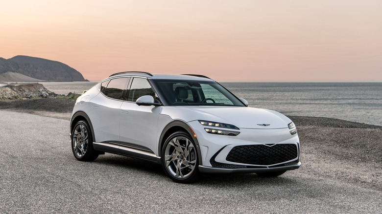 A front three quarters shot of a white GV60 parked in front of the ocean and oceanside cliffs at sunset