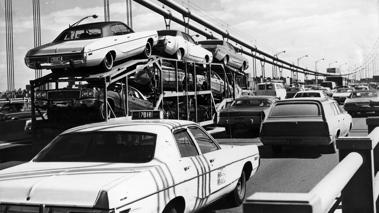 circa 1975: American cars on a road and a car transporter