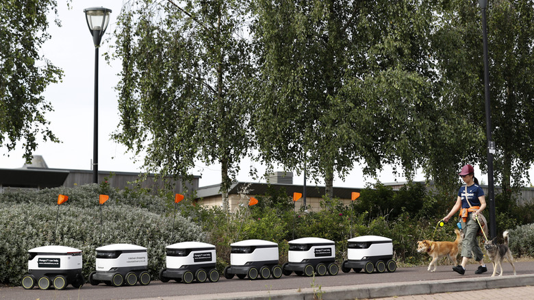 A woman walks dogs past Starship delivery robots waiting for orders during a visit from the Labour Leader Keir Starmer on July 23, 2020 in Milton Keynes, England.