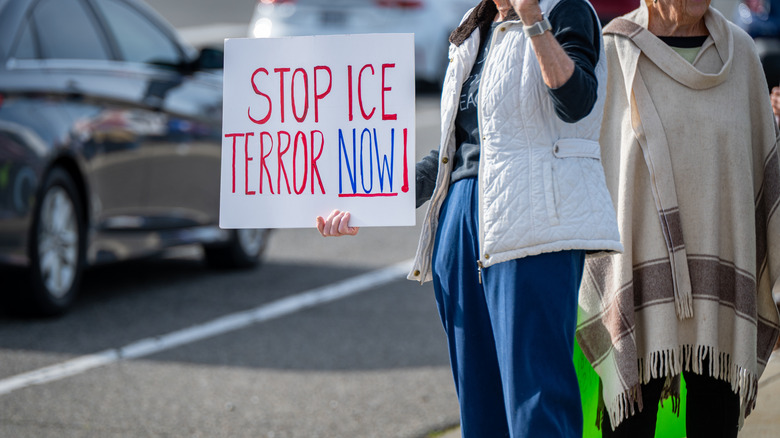 A woman stands along the side of Bell Road holding a "Stop ICE Terror Now" sign as a vehicle passes by during a local demonstration in Auburn, California.