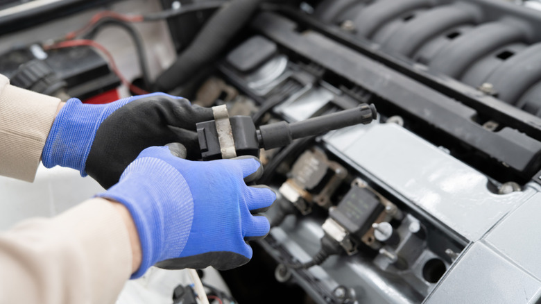 Mechanic holding an ignition coil while working on an engine