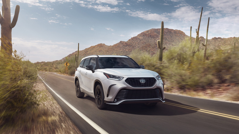 Front 3/4 of a white 2026 Toyota Highlander driving on desert road with cacti