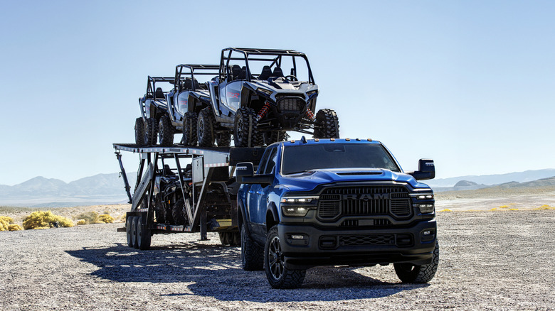 A 2027 Ram Power Wagon with Cummins diesel and a trailer full of ATVs driving in the desert