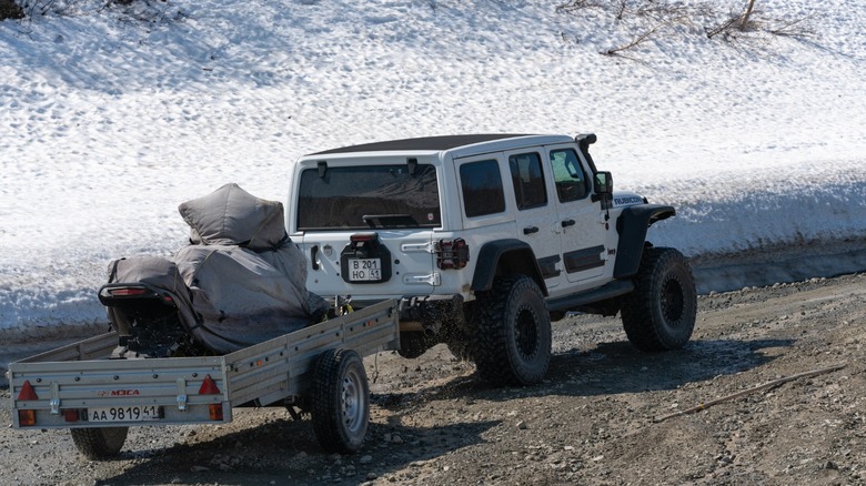 White Jeep Rubicon towing snowmobile on a trailer
