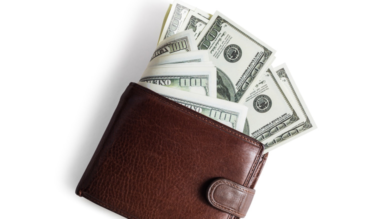 A brown wallet with money sticking out against a white background